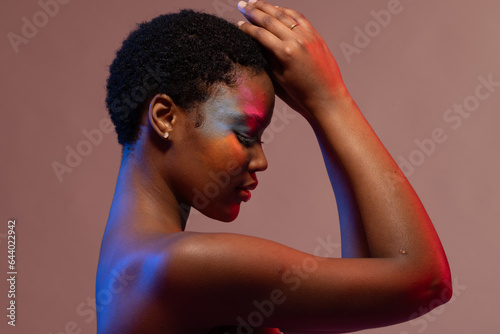 African american woman with short hair and colourful make up touching head in blue and red light
