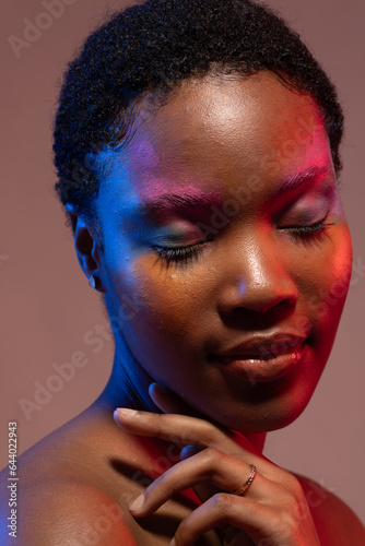 African american woman with short hair and colourful make up touching shoulder with eyes closed