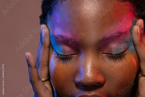 African american woman with short hair and colourful make up touching temples with eyes closed
