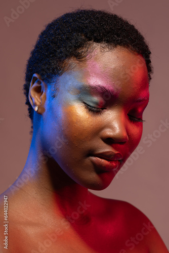 African american woman with short hair and colourful make up with eyes closed in blue and red light