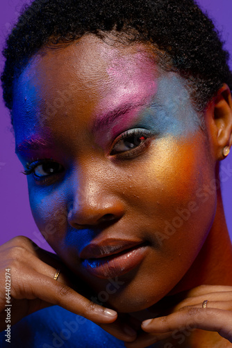 African american woman with short hair, colourful make up and hands under chin