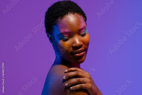 African american woman with short hair and colourful make up looking down with hand on shoulder