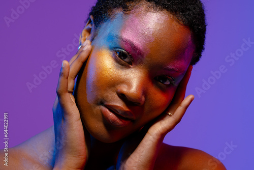 African american woman with short hair and colourful make up touching face