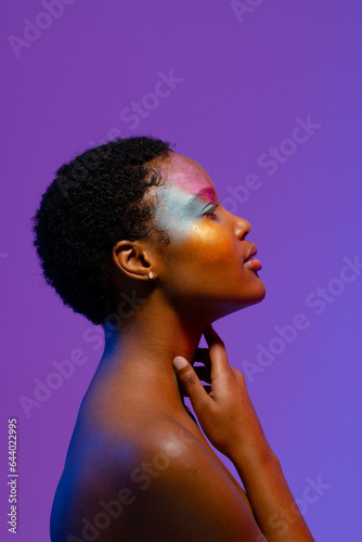 African american woman with short hair and colourful make up touching neck, with copy space