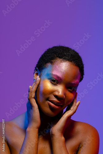 African american woman with short hair and colourful make up touching face, copy space