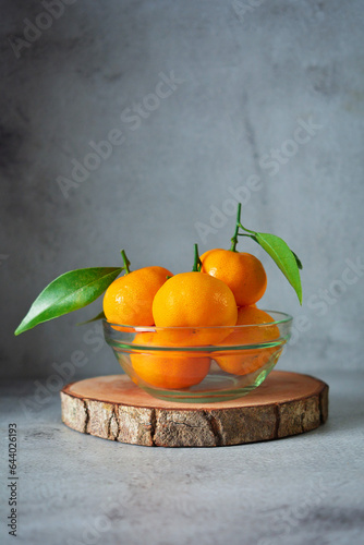 bunch of fresh orange fruits in a glass bowl. mandarin orange fruits on grey and texture background 