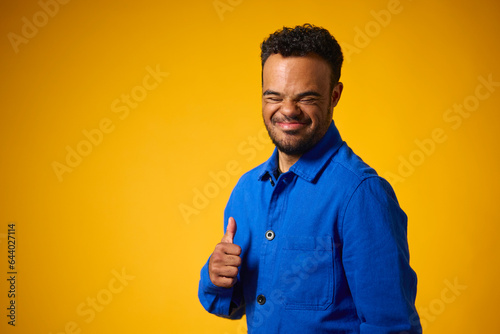 Studio Portrait Of Man With Down Syndrome Standing Against Yellow Background Giving Thumbs Up photo