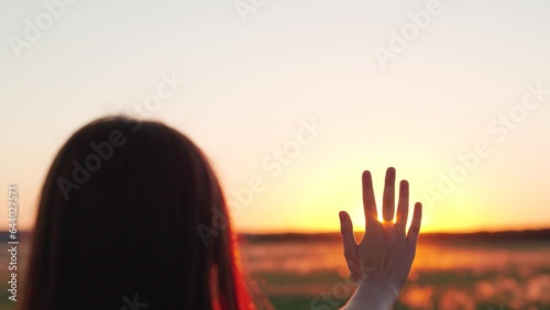 Glare of sunset on fingers of young woman. Silhouette of hand in sun, Happy girls stretches her hand to sun. Prayer of woman, religion of world. Girl travels at sunset. Girl walk at sunset. Prayer god