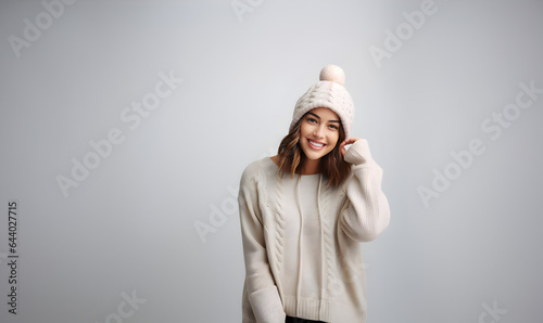Jeune femme souriante portant un pull et un bonnet en laine blanc sur un fond gris clair