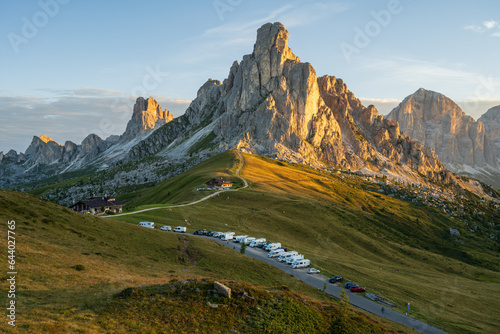 Sunrise at Passo Giau with road and parked cars and campers with sun shining at meadow and peaks in  the background during summer morning in august