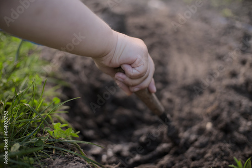 Little kids arm holding tiny shovel digging a hole in dark ground