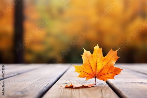 Autumn maple leaf on wooden table in front of blurred background.