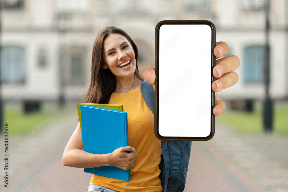 Educational Offer. Beautiful Smiling Female Student Demonstrating Blank Smartphone While Standing Outdoors