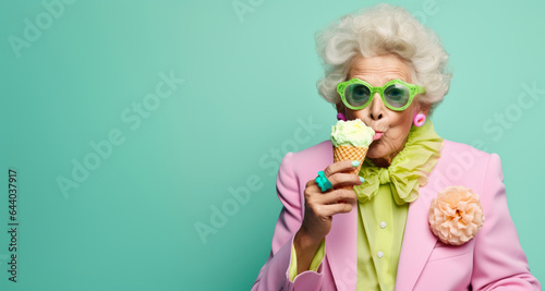 Old senior charming lady in pastel color clothes eat an ice cream on cone. Funny melting scene with food an older aged woman. The background is mint green, copy space.