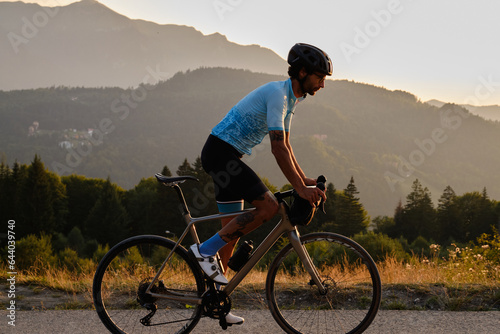 A fit male cyclist practicing on a gravel road at sunset. He is riding a gravel bike with a view of the mountains. Bucegi Mountains, Romania photo