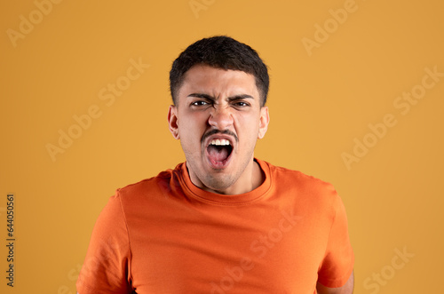 Human reactions concept. Angry brazilian man shouting, screaming loud, expressing negative emotions, yellow background