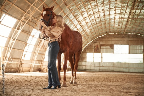 Full height photo. Beautiful young woman is with horse indoors