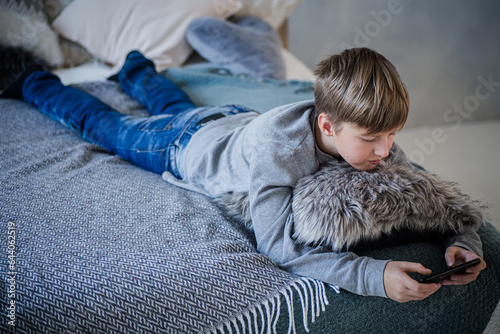 Fényképezés Little boy playing games on phone while lying on bed