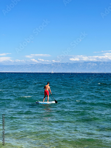 A man floats on a surfboard. Concept: Water sports, entertainment at sea. A young guy stands on a surfboard in the sea. © Сергій Колесніков