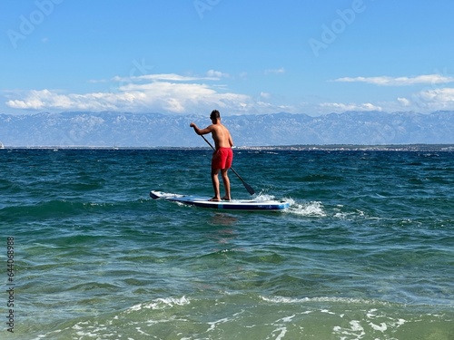 A man floats on a surfboard. Concept: Water sports, entertainment at sea. A young guy stands on a surfboard in the sea.