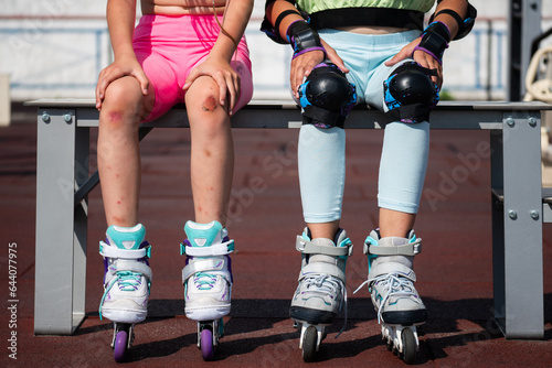 schoolgirls are sitting on a bench after roller skating. girls in protective equipment knee pads and a girl with a trauma on the skin after fall photo