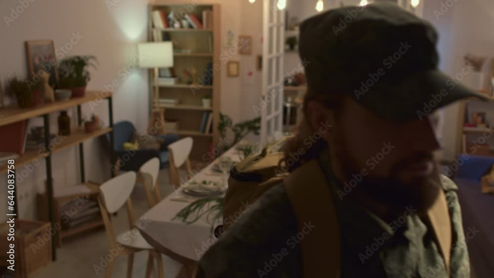 Portrait of serious military man in camouflage uniform with backpack looking at camera and then leaving cozy living room in festive table background Portrait of serious military man in camouflage uniform with backpack looking at camera and then leaving cozy living room in festive table background