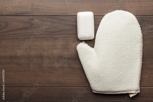 Bath glove with soap bar on the table. Shower glove and bar of soap on wooden background. Flat lay photo of bath glove with copy space.