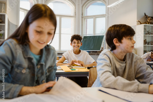 Portrait of happy schoolboy sitting at desk with friends in classroom photo