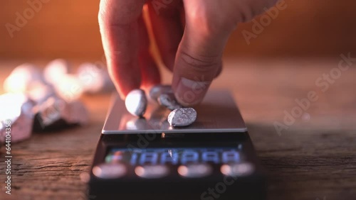 man's hand is placing a lump of platinum or silver or rare earth mineral to be weighed