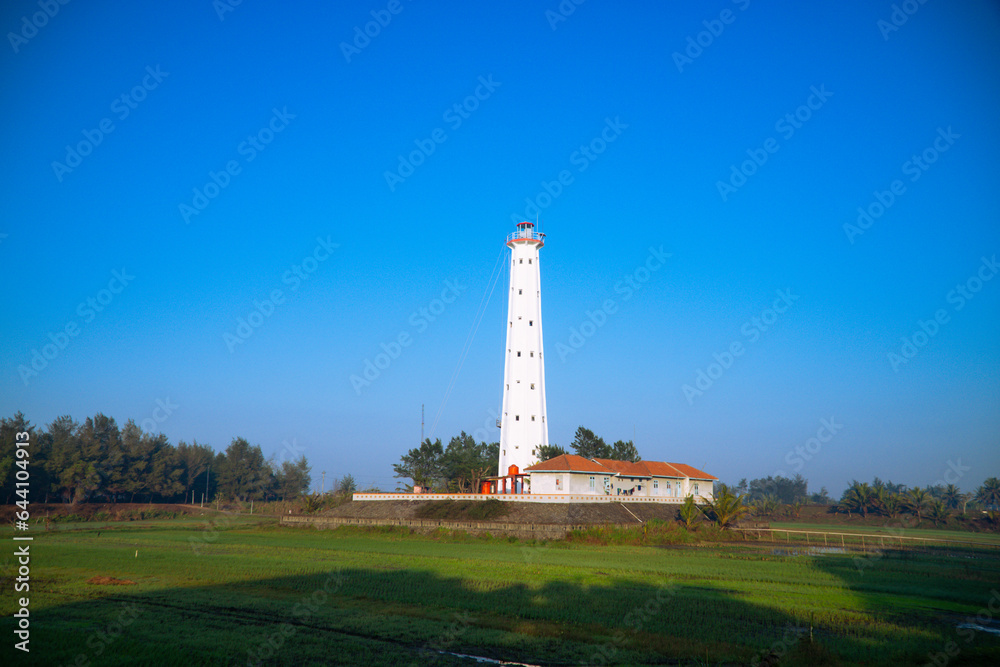White lighthouse with green meadow on foreground and clear blue sky - Ketawang Beach, Indonesia