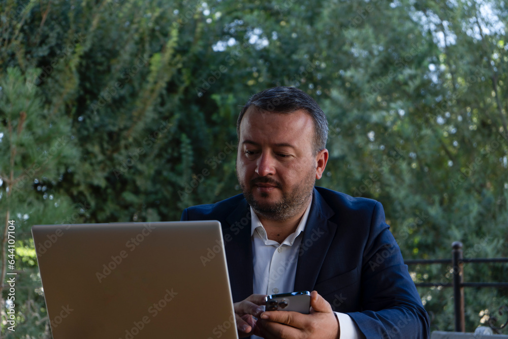 a man working in his laptop with strange face, mature business man in an outdoor ambition working in laptop ,blue coat suit,multiracial asian, successful businessman. a man working in his laptop with strange face, mature business man in an outdoor ambition working in laptop ,blue coat suit,multiracial asian, successful businessman.