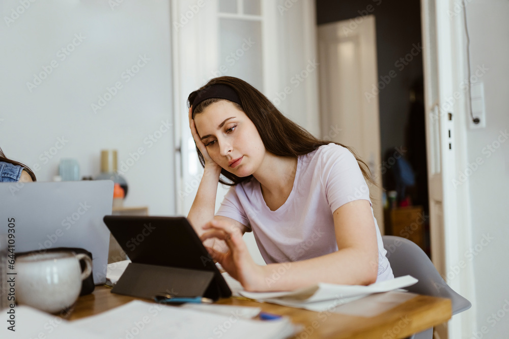 Bored young woman using digital tablet while studying at table Bored young woman using digital tablet while studying at table