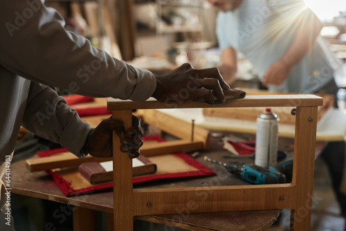 Close up of young black man sanding wooden furniture in carpentry workshop, copy space