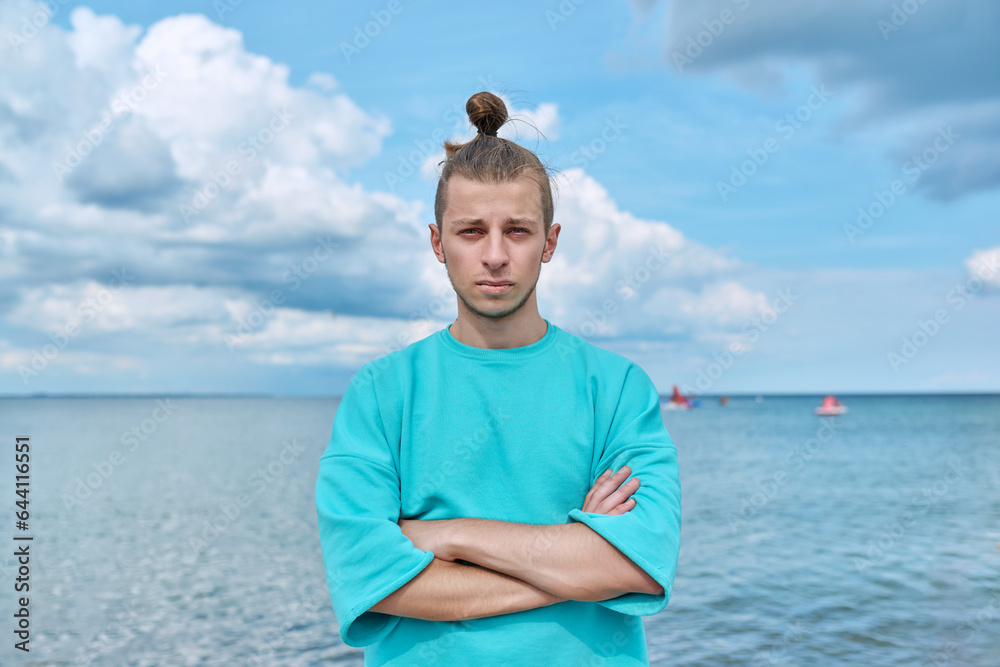 Confident young male with crossed arms looking at camera, sky sea background