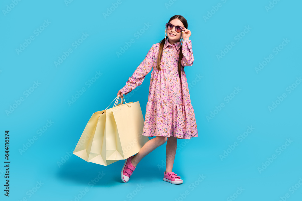 Full body photo of little young schoolgirl kid holding bags fashion discount look mockup sunny weather isolated on blue color background Full body photo of little young schoolgirl kid holding bags fashion discount look mockup sunny weather isolated on blue color background