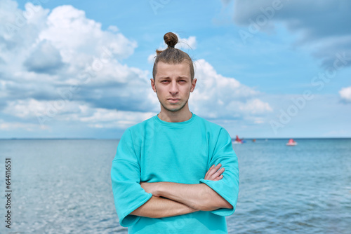 Confident young male with crossed arms looking at camera, sky sea background