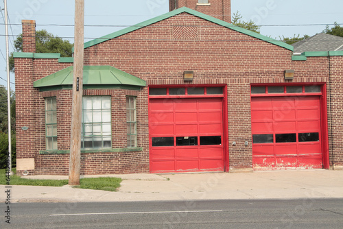 fire department station small boutique vintage brown burgundy brick with two red garage doors with road in front, close up photo