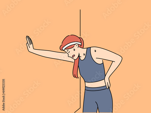 Tired woman runner with sweat on face, leaning against wall and trying to catch breath after long run. Young girl runner needs help of trainer due to excessive fatigue after workout.