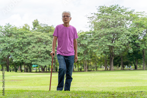 Full length profile shot of a senior man walking with a cane in a park. Elderly old man with walking stick standing in a public park.