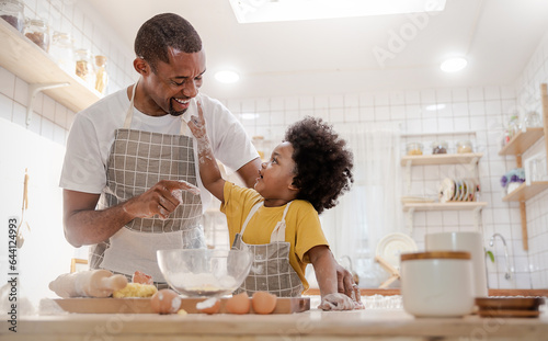 Portrait of African American dad little son having fun in kitchen home, baking pastry in modern kitchen together, kneading Dough prepare cookie pizza. Love fun make homemade food hobby or leisure time