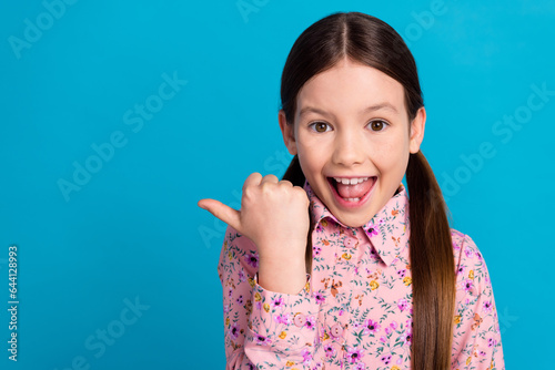 Photo of pretty schoolgirl finger point empty space excited scream wear trendy pink flower print outfit isolated on blue color background