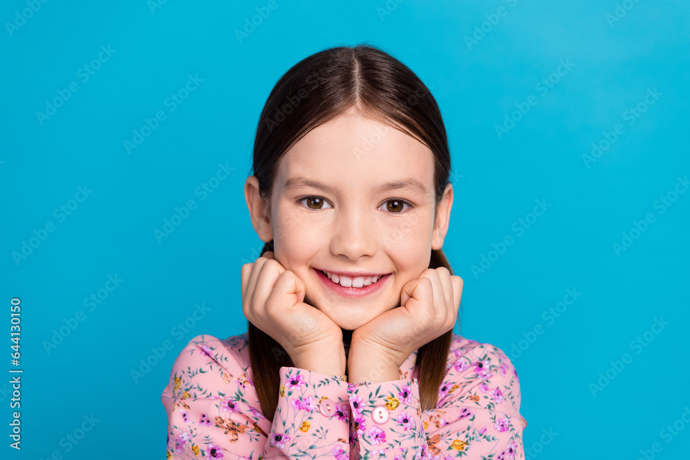 Photo portrait of cute little girl fists touch cheeks admiring wear trendy pink flower print clothes isolated on blue color background Photo portrait of cute little girl fists touch cheeks admiring wear trendy pink flower print clothes isolated on blue color background