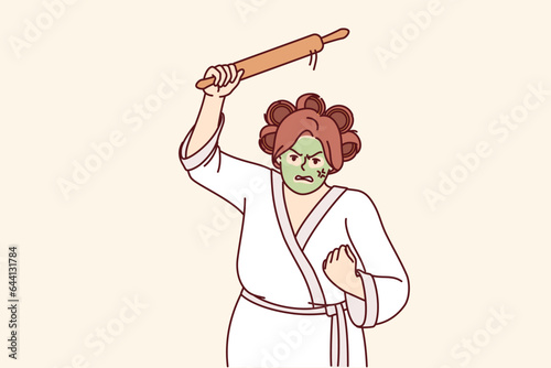 Aggressive woman holding rolling pin and threatening to be beaten, dressed in bathrobe with curlers and cosmetic face mask. Funny housewife with unbalanced psyche demonstrates aggressive mood