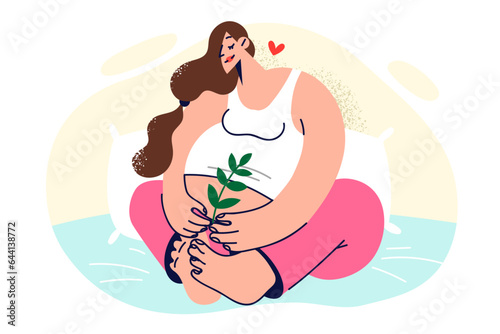 Pregnant woman sits on bed with smile and holds twig of plant, dreaming of happy motherhood