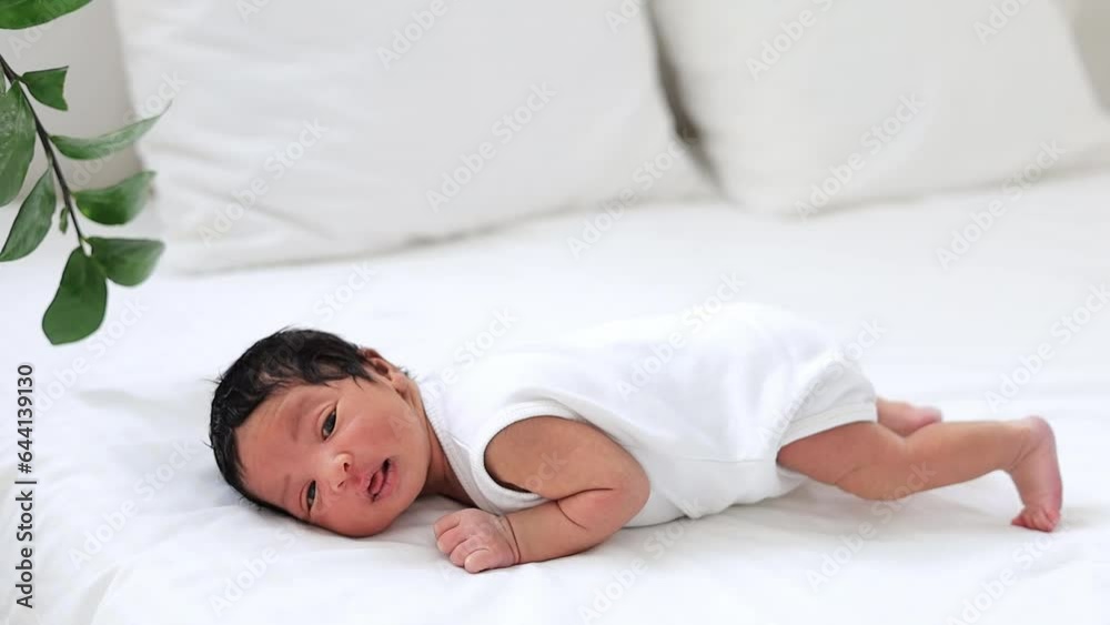 portrait of a newborn black African-American baby funny showing tongue, a small dark-skinned baby close-up lying on the bed on his tummy in the bedroom waking up or falling asleep in a white bodysuit portrait of a newborn black African-American baby funny showing tongue, a small dark-skinned baby close-up lying on the bed on his tummy in the bedroom waking up or falling asleep in a white bodysuit