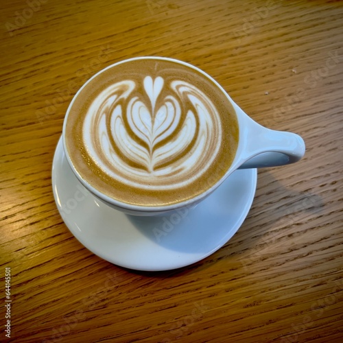 Latte coffee with attractive pattern in the cream on top, white ceramic cup on wooden table