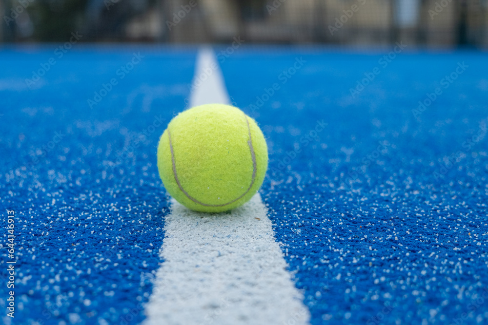 selective focus, a yellow ball over the line of a blue paddle tennis court