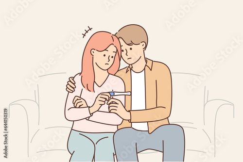 Problem of infertility in man and woman sitting on couch with negative pregnancy test in hands