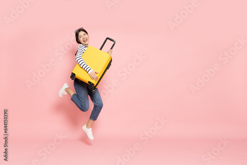 Asian happy woman jumping with yellow suitcase isolated on pink background, Tourist girl having cheerful holiday trip concept
