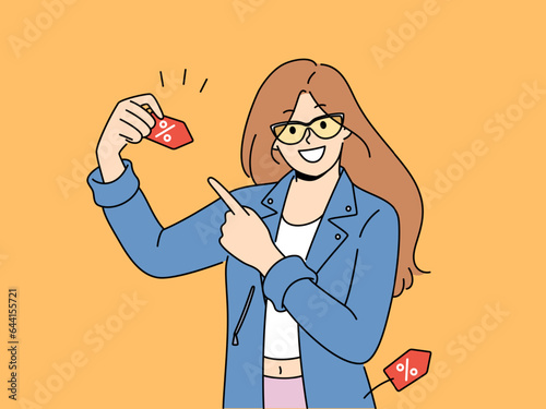 Happy woman announces discounts for shopping and buying clothes, pointing finger at tag with percentage symbol. Girl promoter invites to sale in mall and promises big discounts on black friday